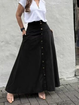 Front view of a woman styling a high-waisted button-front A-line utility maxi skirt with front panel seams and pockets.
